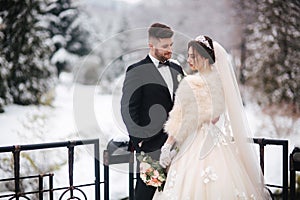 Newlyweds in witer park are walking around. Handsome groom and beautiful bride surrounded by snow. Winter wedding