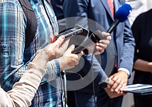 News conference, journalists with microphones and digital voice recorder interviewing politician or business person photo