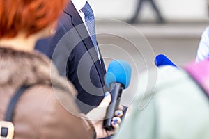 News conference, journalists with microphones interviewing politician or business person during media event