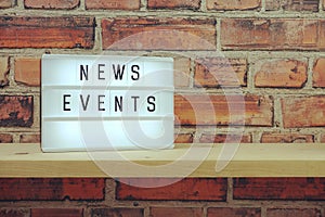 News Events word in light box on brick wall and wooden shelves background