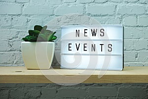 News Events word in light box on brick wall and wooden shelves background