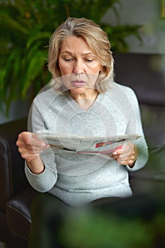 News, press, media, holidays and people concept - woman reading newspaper at home.