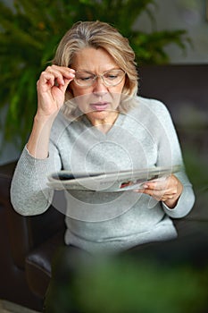 News, press, media, holidays and people concept - woman reading newspaper at home.