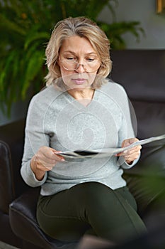 News, press, media, holidays and people concept - woman reading newspaper at home.