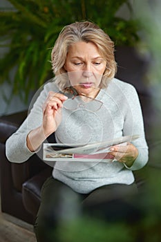 News, press, media, holidays and people concept - woman reading newspaper at home.