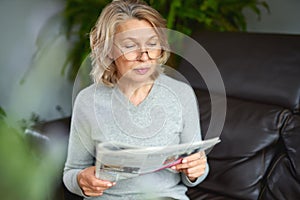 News, press, media, holidays and people concept - woman reading newspaper at home.