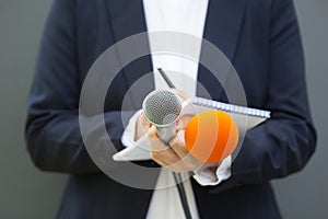 News reporter or journalist at press conference, holding microphone and writing notes