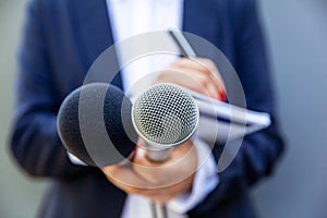 Female journalist at news conference or media event, writing notes, holding microphone