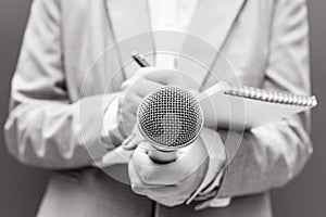 Female journalist at news conference or media event, writing notes, holding microphone