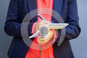 Female journalist at news conference or media event, writing notes, holding microphone