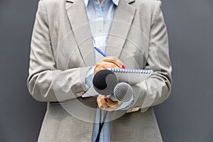 News reporter or TV journalist at press conference or media event, holding microphone and writing notes. Broadcast journalism.