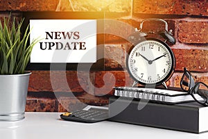 NEWS UPDATE text with alarm clock, books and vase on brick background