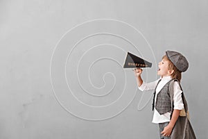 Newsboy shouting against grunge wall background. Boy selling newspaper