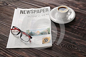 Newspaper with glasses and cup of coffee on wooden table