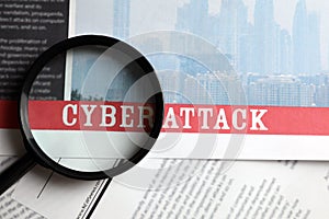 Newspaper with headline CYBER ATTACK and magnifying glass, top view