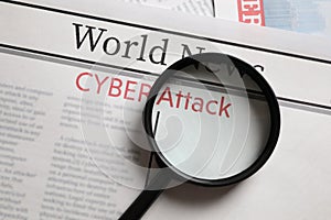 Newspaper with headline CYBER ATTACK and magnifying glass, top view