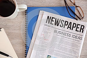 Newspaper, notebooks and cup of coffee on wooden table