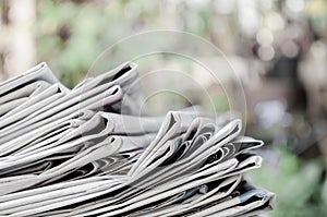 Newspapers folded and stacked on the table with outdoor garden or green background. Closeup newspaper and selective focus image. T