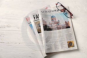 Newspapers and glasses on white wooden background