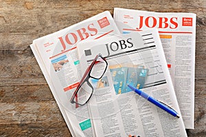 Newspapers with headlines JOBS and glasses on wooden background