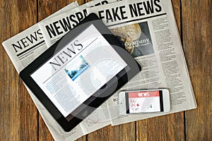 Newspapers, tablet computer and phone with news on screen on wooden table photo