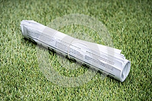 Newspapers Tied With Rubber Band On Green Grass