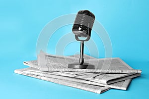 Newspapers and vintage microphone on light blue background. Journalist`s work