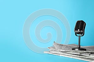 Newspapers and vintage microphone on light blue background, space for text. Journalist`s work