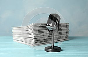 Newspapers and vintage microphone on light blue wooden table. Journalist`s work