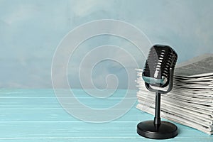 Newspapers and vintage microphone on light blue wooden table, space for text