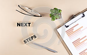 NEXT STEPS text on wooden block with chart and glasses, business concept