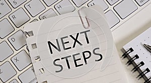 Next Steps text on wooden desk with tablet pc and keyboard.