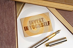 Next to the books lies a pen and a sign with the inscription - INVEST IN YOURSELF