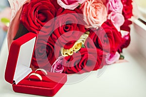 Next to the bouquet of the bride lies a pair of gold wedding rings in a red velvet box.