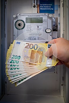 next to an electric meter is held a lot of two hundred euro banknotes