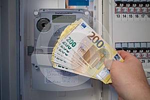 next to an electric meter is held a lot of two hundred euro banknotes