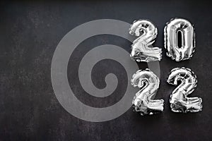 Nflatable shiny silver numbers of the new year 2022 on a dark grey or black background. Copy space