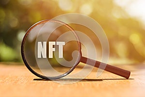 NFT concept. Magnifier glass with text on the green background in sunlight