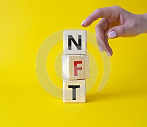 NFT - non-fungible token symbol. Concept word NFT on wooden cubes. Businessman hand. Beautiful yellow background. Business and NFT