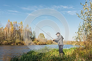 Ðngler in a jacket with a fishing rod stands on the river bank. Fishing on the river