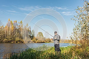 Ðngler in a jacket with a fishing rod stands on the river bank. Fishing on the river