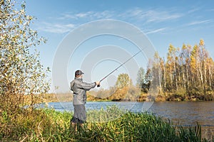 Ðngler in a jacket with a fishing rod stands on the river bank. Fishing on the river