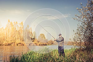 Ðngler in a jacket with a fishing rod stands on the river bank. Fishing on the river