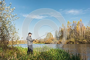 Ðngler in a jacket with a fishing rod stands on the river bank. Fishing on the river