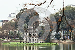 Ngoc Son Temple on Hoan Kiem Lake with trees in background and branches in foreground in Hanoi, Vietnam