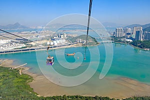 Ngong Ping Cable car with tourists over harbor, mountains and city background, to visit the Tian Tan or the Big Buddha located at