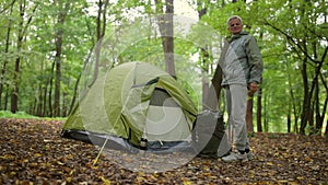 Nice aged man standing in the forest near his tent