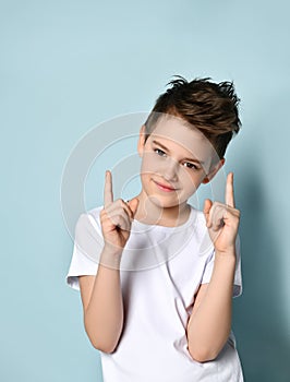 Lindo pequeno chico en blanco buscando adelante sonrisa introducción ambos dedos arriba 