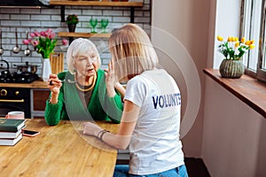 Nice-appealing social worker consoling aging granny in green wool cardigan.