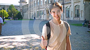 Nice asian boy is demonstrating like gesture while standing straight on empty street, sun shines surrounds view